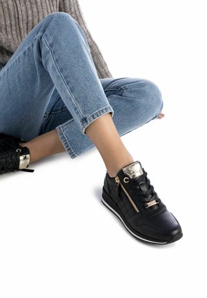 Zapatillas de cuero negras con un acento metálico dorado, que cuentan con un cierre de cremallera, panel lateral texturizado y suela de goma plana.