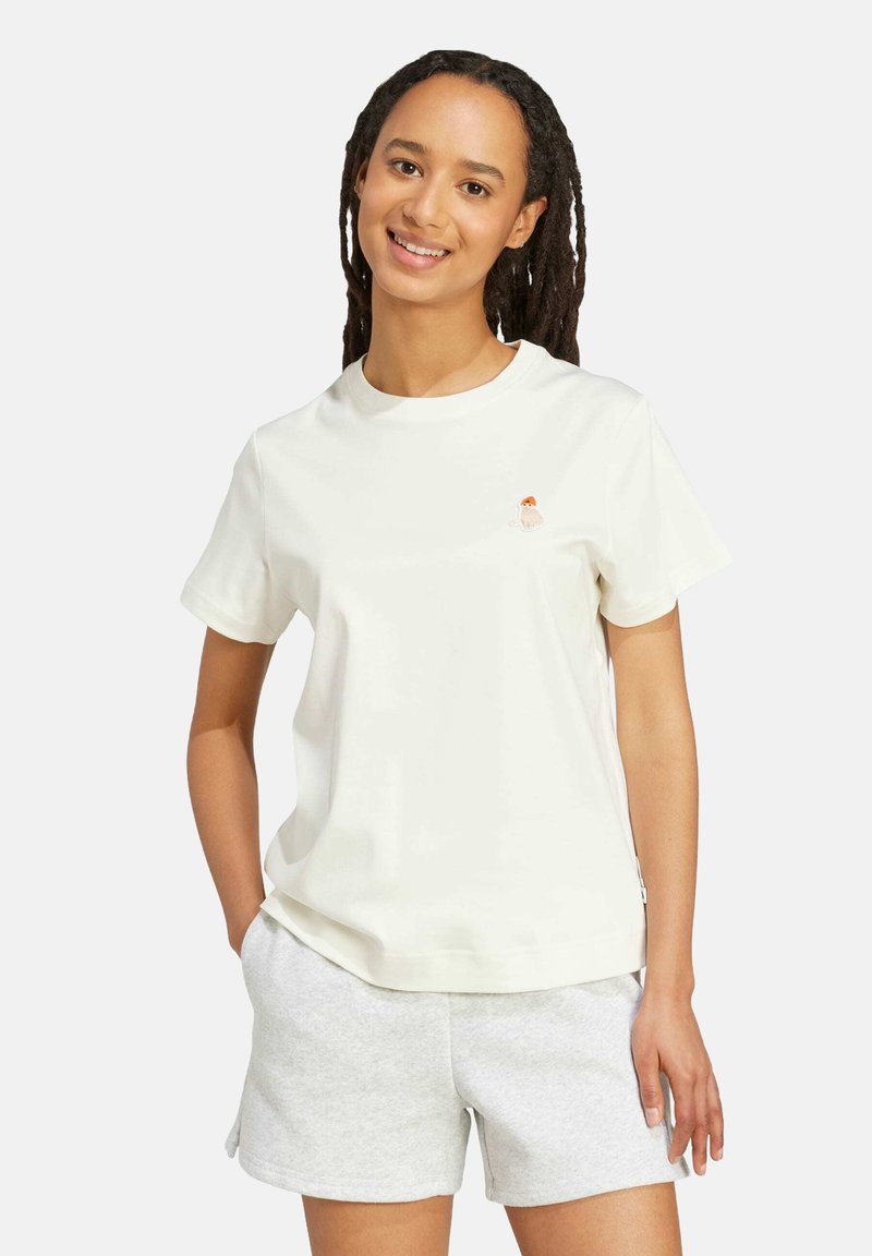 Weißes Baumwoll-T-Shirt mit kurzen Ärmeln und Rundhals, mit einem kleinen, orange- und braun gestickten Detail auf der Brust. Kombiniert mit grauen Shorts.