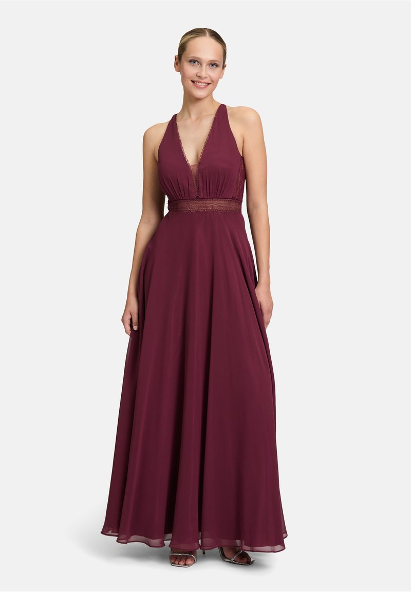 Robe de soirée bourgogne avec un col halter, un corsage ajusté et une jupe fluide. Détail de taille texturé ; tissu transparent qui tombe élégamment.