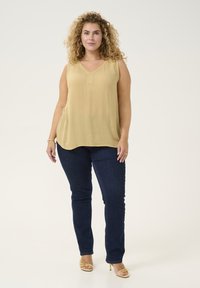 Top sin mangas de color amarillo claro con un sutil escote en V, combinado con jeans ajustados de color azul oscuro y sandalias de tacón alto amarillas. Textura de tela lisa.