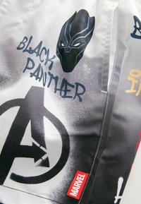 Mustaa kangasta, jossa on erilaisia graafisia painokuvia, mukaan lukien Black Pantherin maski, Avengers-logo ja teksti. Punainen "MARVEL" -labeli näkyvissä.
