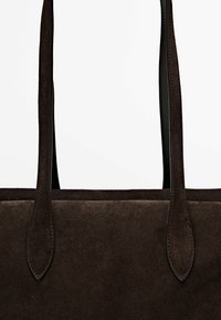 Dunkelbraune Wildleder-Shopper-Tasche mit langen, schmalen Schulterriemen und sichtbaren Nähten vor einem schlichten Hintergrund.