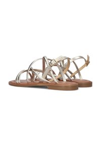 Metallische zilveren sandalen met kruislings bandjes, vlakken bruine zool en verstelbare enkelgesp. Gladde textuur en minimalistisch ontwerp.