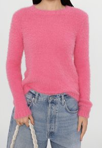 Puszysty różowy sweter z długimi rękawami i okrągłym dekoltem, w połączeniu z jasnoniebieskimi dżinsami o wysokim stanie. Zauważalny kontrast faktury i koloru.