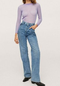 Vaalean violetti, puoliläpinäkyvä, pitkähihainen paita, jossa on teksturoitu kuvio, yhdistettynä korkeavyötäröisiin, haalistuneisiin sinisiin leveälahkeisiin farkkuihin ja mustiin teräväkärkisiin nilkkureihin.