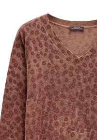 Brązowy sweter z dzianiny z dekoltem w serek, z teksturowanym wzorem w czerwone i ciemnobrązowe plamy. Miękki materiał i ściągacz przy kołnierzu.