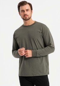 Camicia a maniche lunghe in cotone verde oliva con colletto rotondo e orlo dritto. Il modello presenta maniche aderenti e una silhouette rilassata.