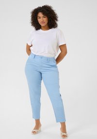 Pantalones ajustados de color azul claro con una silueta entallada, trabillas para cinturón y cierre de botón. Combinados con una camiseta blanca de manga corta y lisa.
