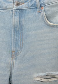 Ljusblå denimjeans med en metallknapp, framficka, bälteloopar och en slitning nära nedre högra kanten.