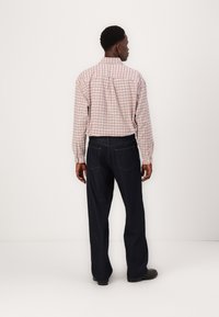 Cămașă cu mâneci lungi în carouri, de culoare roz deschis și alb, asortată cu pantaloni din denim de culoare albastru închis. Cămașa are guler cu nasturi și șliț la spate.