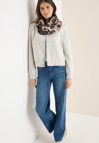 Světlounce šedý zkrácený kardigan se zapínáním na druky, kombinovaný s modrými širokými džínami. Černobéžový leopardí šátek přehozený kolem krku.