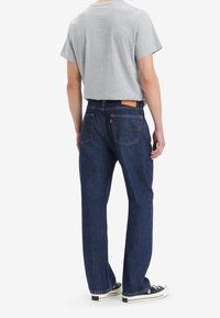 T-shirt gris court à manches courtes, associé à un jean en denim bleu foncé, avec une coupe droite et deux poches arrière. Baskets noires.