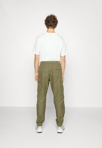 Olivinvihreät cargo-housut, joissa on joustava vyötärönauha, sivutaskut ja rento istuvuus. Yhdistetty yksiväriseen valkoiseen t-paitaan, nähtynä takaa.