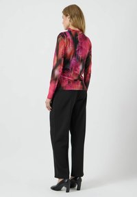 Zwarte broek gecombineerd met een lange mouw top met een bloemenpatroon in tinten roze en zwart, gladde textuur en aangesloten stijl.