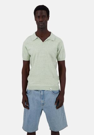 Polo shirt verde pallido a maniche corte con colletto ampio abbinato a pantaloni corti in denim azzurro chiaro. Tessuto in cotone, vestibilità rilassata e design essenziale.