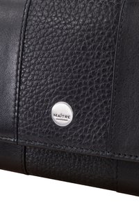 Borsa nera in pelle caratterizzata da pannelli testurizzati e lisci, con un logo "MAÎTRE" in argento embosso su un accento circolare.