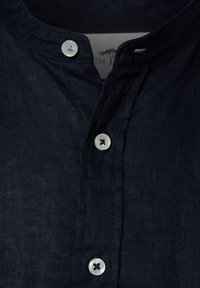 Donker marineblauw linnen shirt met een mandarinnekraag, voorzien van twee knopen—één met een blauwe accenten—die een textuur van de stof blootlegt.
