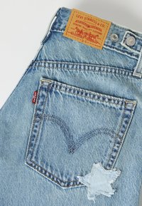 Μπλε τζιν Levi's που δείχνει πίσω τσέπη, δερμάτινη ετικέτα μάρκας, μεταλλικό κουμπί και ένα φθαρμένο μπαλώμα σε σχήμα αστεριού.