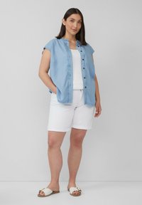 Hellblaues Denim-Hemd mit kurzen Ärmeln, weißes Tanktop, weiße, hochgekrempelte Shorts und bequeme, beigen Slidesandalen mit dekorativem Akzent.