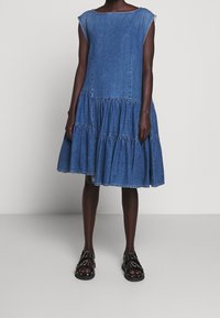 Džínové šaty s volným střihem, krátkým rukávem a rozšířenou sukní ve vrstvách. Disponují světle modrou barvou a surovým okrajem u výstřihu.