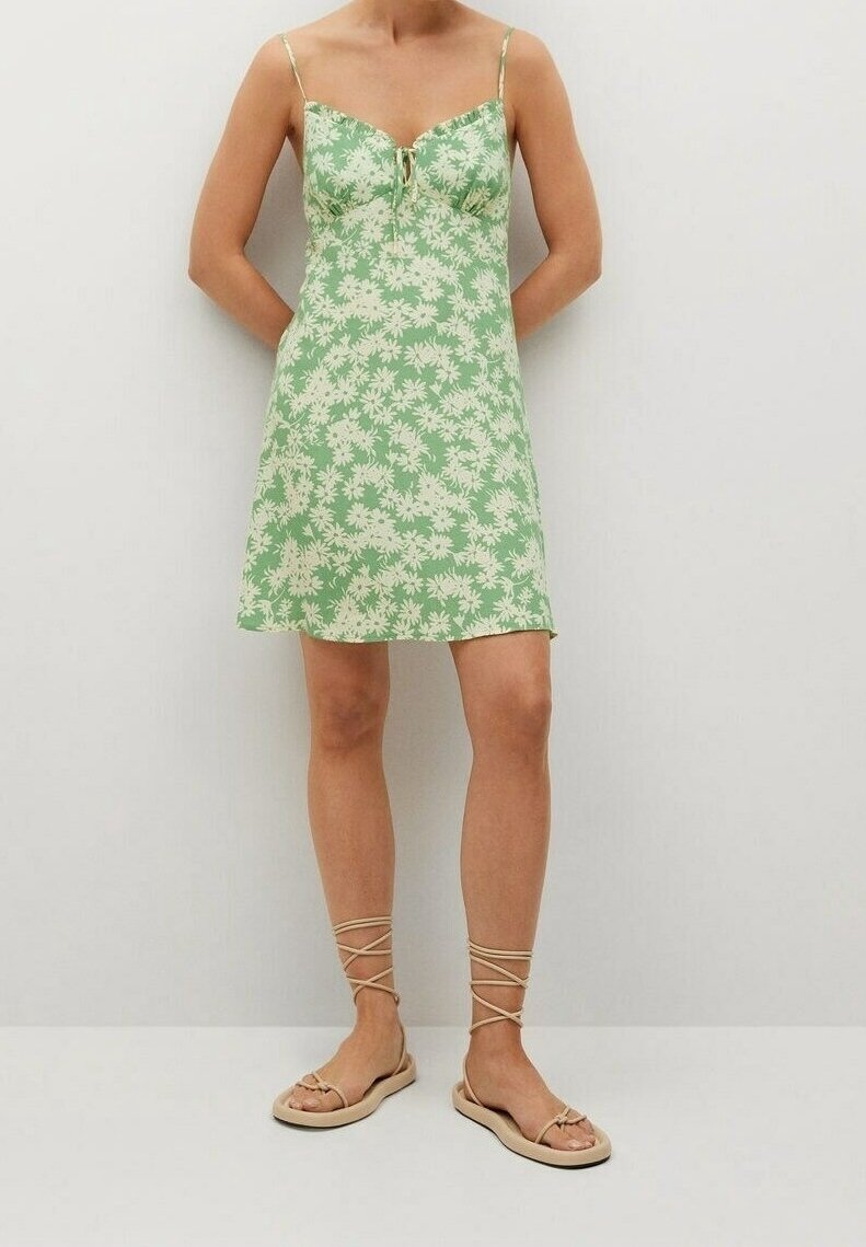 Vestido floral verde con tirantes finos, presenta un cuerpo ajustado, detalle de ojal y un dobladillo acampanado, combinado con sandalias planas y con tiras.