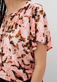 Kurzärmlige Bluse in Rosa mit einem braunen und schwarzen abstrakten Muster, ausgestattet mit Falten und einem Ausschnitt mit Schlüsselring. Weicher und leichter Stoff.