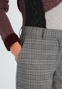 Gestreepte grijze broeken met een.getailleerde pasvorm, voorzien van zijzakken en een gladde textuur, gecombineerd met een meerkleurige gebreide trui.