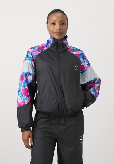 Veste de sport noire avec des manches à motifs tie-dye colorés, col montant et fermeture éclair. Présente un logo sur la poitrine et des poignets élastiques.