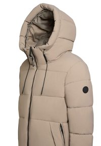Béžová péřová bunda s vysokým límcem a převelkým kapucí. Obsahuje zapínání na zip, stahovací šňůrky a černou nášivku s logem na rukávu.