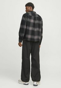 Sort og grå ternet flannel-skjorte med knaplukning ved håndleddene, båret over løstsiddende sorte bukser og lette træningssko.