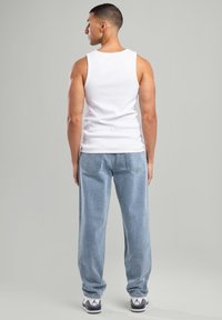 Top in cotone bianco abbinato a jeans in denim azzurro chiaro. I jeans hanno una vestibilità ampia e tasche posteriori tradizionali; le scarpe sono in bianco e nero.