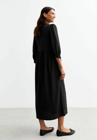 Black midi dress with puffed sleeves, gathered waist, flowing skirt, and textured fabric. Worn with black ballet flats.