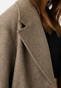 Blazer oversized in misto lana marrone con rever e superficie testurizzata. Presenta una silhouette pulita e strutturata.