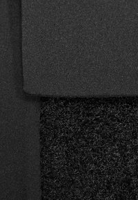 Schwarzer Stoff mit einer glatten, matten Oberfläche und einem klettartigen Material mit einer flauschigen, gewundenen Struktur. Zwei verschiedene Texturen sind sichtbar.