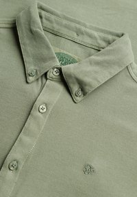 Lichtgroen overhemd met knopen, een gestructureerde stof, een knoopsluiting bij de kraag en een klein geborduurd logo op de borst.