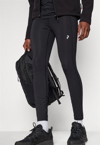 Svarta träningsleggings med en slät textur och kontrasterande sömdetaljer. Kombinerat med en svart ryggsäck och mörka sneakers.
