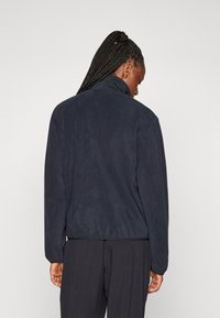 Marineblaue Fleecejacke mit hohem Kragen und gerippten Bündchen, weiche Textur und relaxte Passform. Die Rückansicht zeigt keine auffälligen Details.