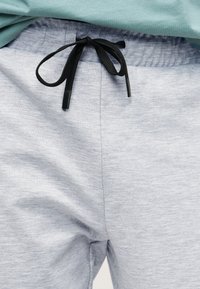 Ανοιχτό γκρι φόρμα με μαύρο κορδόνι δεμένο σε φιόγκο στη μέση, φορεμένο με ανοιχτό τιρκουάζ τοπ.