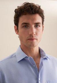 Camicia colletto azzurro con un motivo a righe sottile, patta dei bottoni, dettaglio del colletto interno a contrasto e una texture del tessuto liscia.
