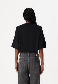 Camiseta negra de corte cropped con mangas anchas, combinada con jeans gris oscuro que presentan un parche con logo en la cintura y dos bolsillos traseros.