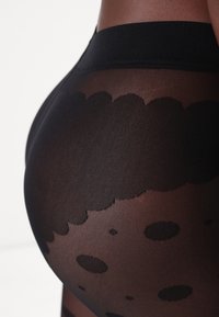 Collant neri con un design trasparente caratterizzato da motivi a nuvola e pois. Il materiale ha una texture liscia e leggermente lucida.