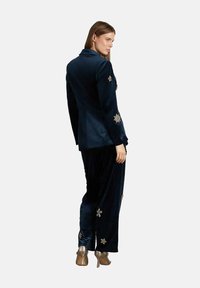 Traje de terciopelo azul marino que incluye una americana entallada con adornos decorativos de estrellas en las mangas y pantalones a juego. Zapatos de tacón alto brillantes.