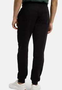 Czarne dresowe spodnie z elastycznym pasem i ściągaczami, z tylną kieszenią. Noszone z białymi trampkami, prezentujące swobodny krój.