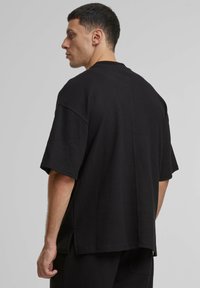 Juoda trumpa rankovė t-shirt, tekstūruota, laisvo silueto su šoninėmis skeltukais ir apvaliu kaklu, rodanti švarų nugaros siūlės dizainą.
