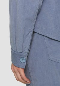 Lichtblauw corduroy shirt met een knoopmanchet, ribbeltextuur en gelaagd ontwerp met zichtbare stiksels en detail van een opgezet zakje.