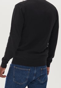 Černá mikina s kulatým výstřihem a dlouhými rukávy, vyrobená z měkké bavlny, vystavená s modrými džínami se zadními kapsami.