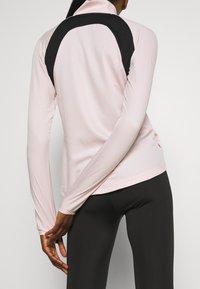 Rosa Langarm-Sportoberteil mit hohem Kragen und schwarzem Rückenpanel. Aus glattem Stoff gefertigt und mit einer figurschmeichelnden Passform, kombiniert mit schwarzen Leggings.