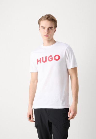 Бяла памучна тениска с отличителен червен логотип "HUGO". Къси ръкави и кръгло деколте; гладка текстура и ежедневен крой.