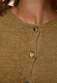 Brun strikket cardigan med rund hals, som har to knapper, teksturert stoff og synlige sømmer langs frontåpningen.