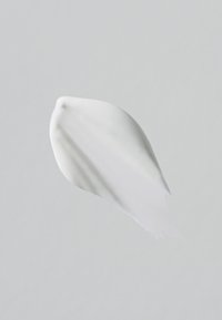 White cream smear with smooth texture on a light gray background, showing subtle ridges and varying thickness.